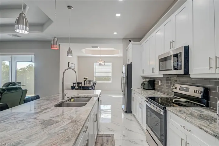 Kitchen with a tray ceiling, stainless steel appliances, light stone counters, white cabinetry, and hanging light fixtures