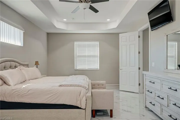 Bedroom with a ceiling fan, a tray ceiling, recessed lighting, and light marble finish floors