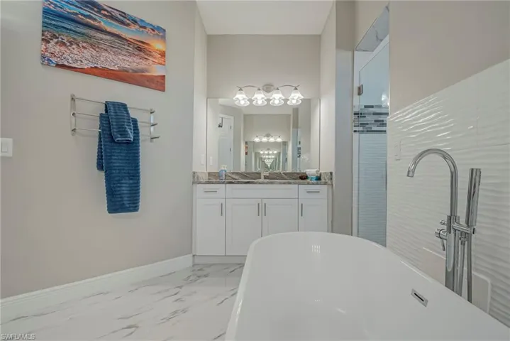 Full bath featuring vanity, a freestanding bath, a stall shower, and light marble finish flooring
