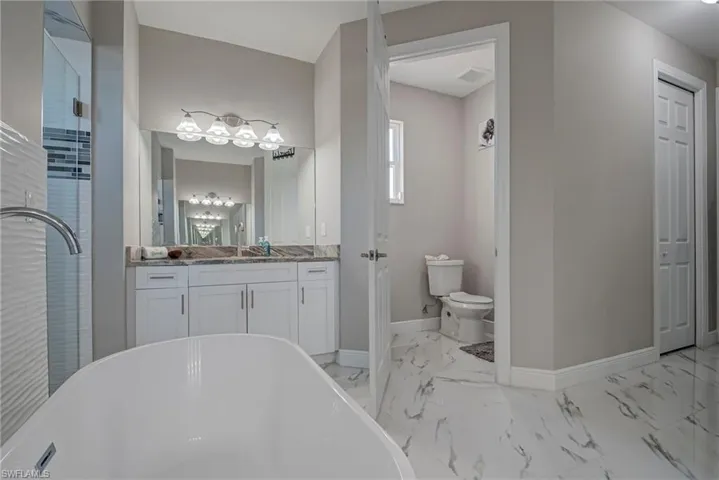 Full bathroom with vanity, a stall shower, a freestanding bath, and light marble finish floors