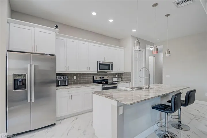 Kitchen with stainless steel appliances, light stone counters, a kitchen breakfast bar, white cabinetry, and light marble finish flooring
