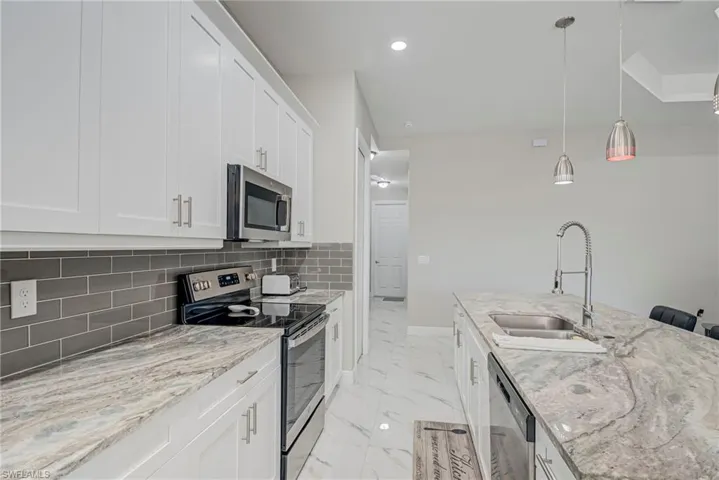 Kitchen with stainless steel appliances, light stone countertops, decorative light fixtures, white cabinetry, and light marble finish floors