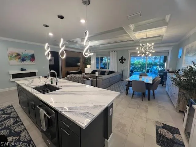 Kitchen with dark cabinets, open floor plan, suspended lighting, coffered ceiling, and ornamental molding