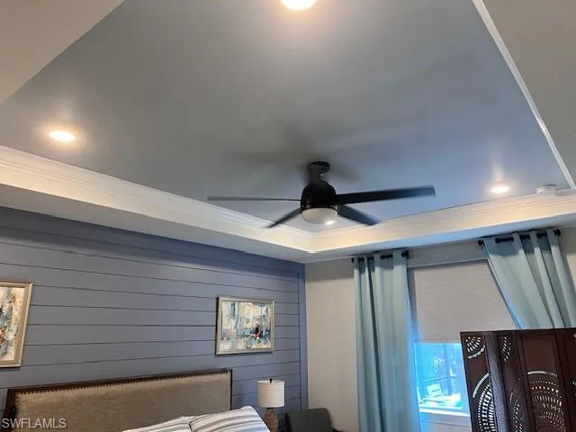 Bedroom with crown molding, recessed lighting, a tray ceiling, wooden walls, and ceiling fan