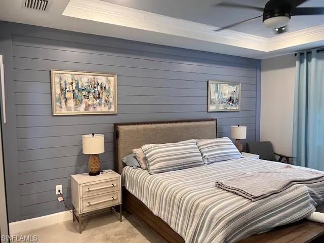 Bedroom featuring wooden walls, a raised ceiling, crown molding, and ceiling fan