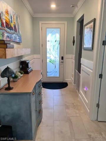 Entryway with wainscoting, a decorative wall, ornamental molding, and tile patterned flooring