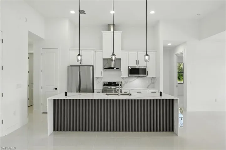 Kitchen with appliances with stainless steel finishes, white cabinets, decorative backsplash, a kitchen island with sink, and wall chimney range hood