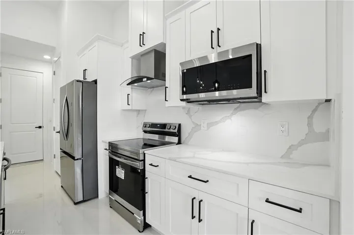 Kitchen featuring stainless steel appliances, wall chimney exhaust hood, white cabinets, backsplash, and light stone countertops