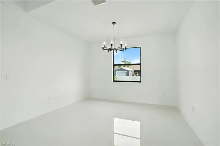 Tiled spare room featuring a chandelier and baseboards