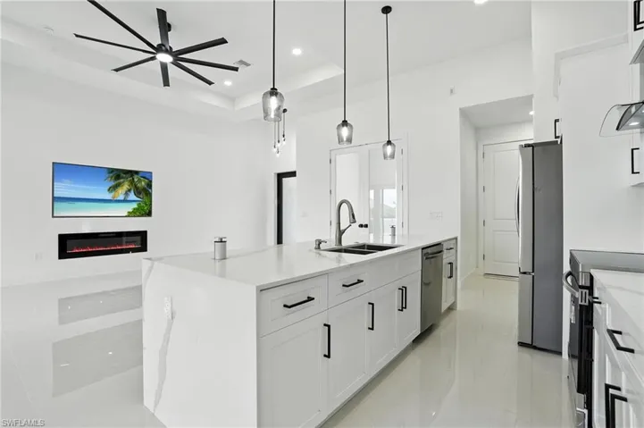 Kitchen featuring appliances with stainless steel finishes, a ceiling fan, open floor plan, white cabinetry, and a glass covered fireplace