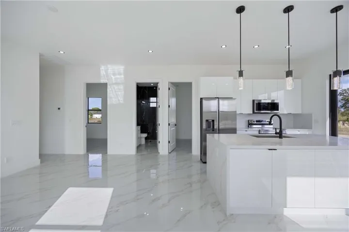 Kitchen with white cabinets, stainless steel appliances, pendant lighting, modern cabinets, and light stone counters