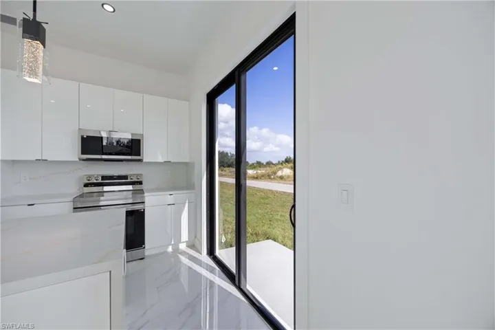 Kitchen with stainless steel appliances, modern cabinets, white cabinets, pendant lighting, and light marble finish floors