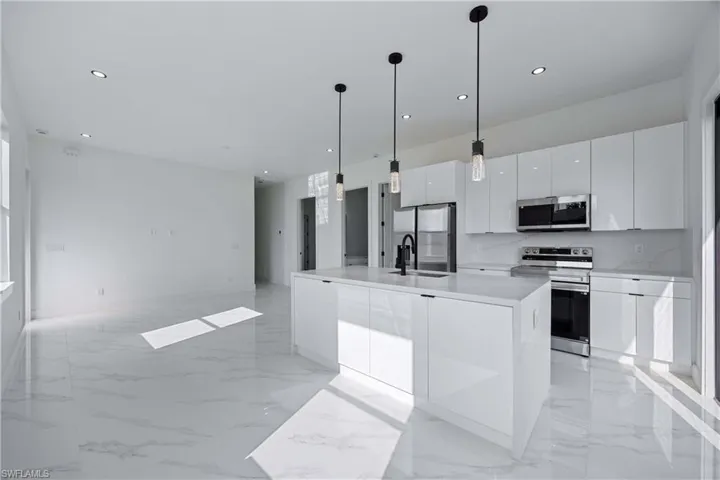 Kitchen featuring stainless steel appliances, white cabinetry, an island with sink, modern cabinets, and pendant lighting