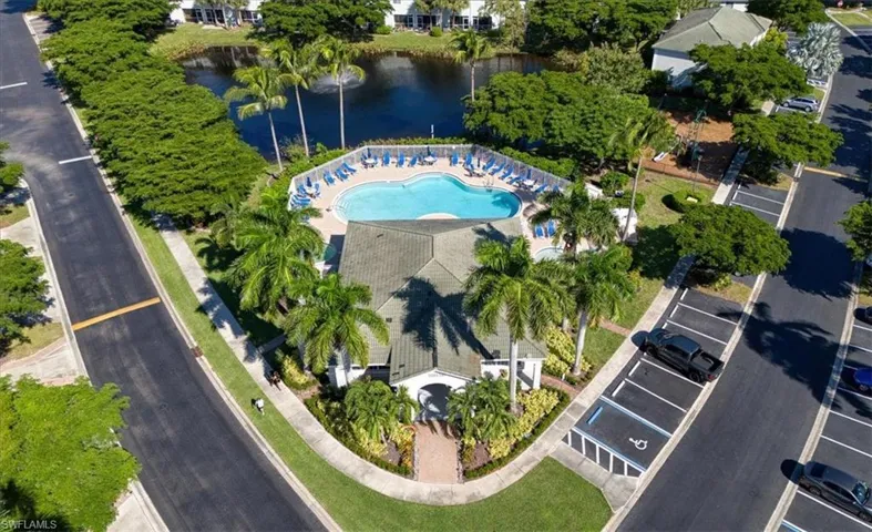 Community clubhouse featuring a swimming pool, spa, and water fountain overlooking a lake with mature palm tree landscaping
