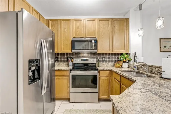 Kitchen featuring light-finish wood cabinetry, speckled stone countertops, a tiled backsplash, stainless steel appliances, and dual pendant lighting