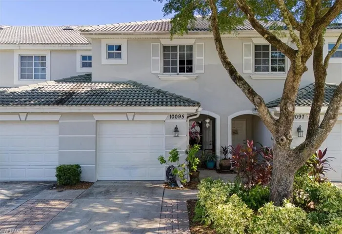 Two-story townhouse exterior featuring a concrete tile roof, stucco facade, decorative window shutters, and attached garage