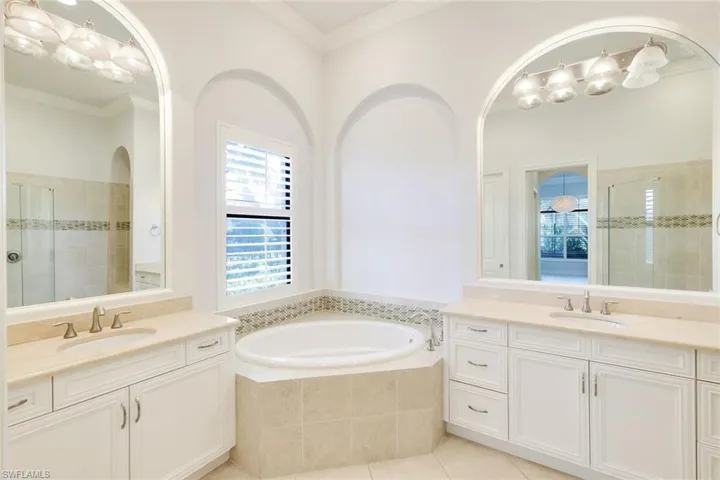 Full bath with a stall shower, light tile patterned floors, two vanities, a garden tub, and crown molding