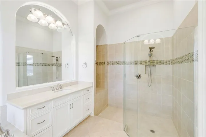 Bathroom featuring vanity, walk in shower, crown molding, and light tile patterned floors