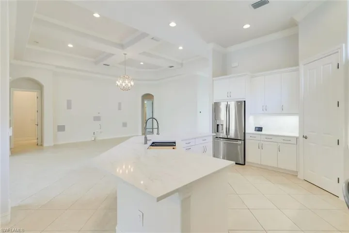 Kitchen featuring arched walkways, white cabinetry, stainless steel refrigerator with ice dispenser, coffered ceiling, and a spacious island