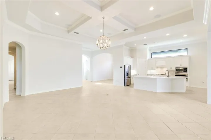Unfurnished living room with arched walkways, coffered ceiling, ornamental molding, hanging lights, and light tile patterned floors