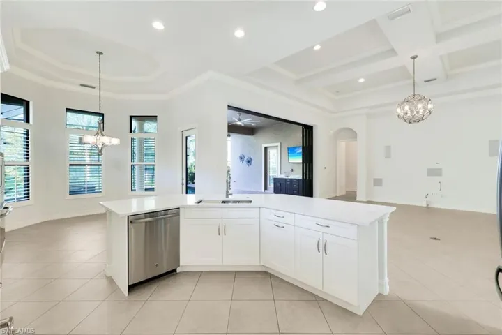 Kitchen featuring hanging lights, white cabinets, an island with sink, open floor plan, and stainless steel dishwasher