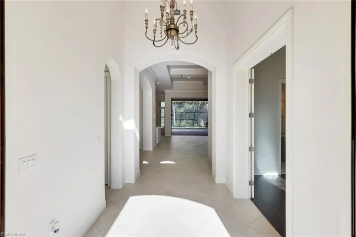 Hallway with arched walkways, suspended lighting, a high ceiling, and light tile patterned floors