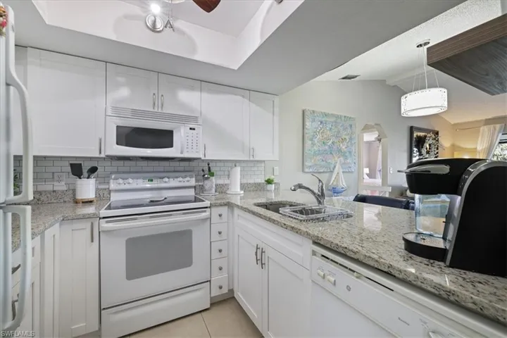 Kitchen with white appliances, white cabinetry, vaulted ceiling, light stone counters, and tasteful backsplash