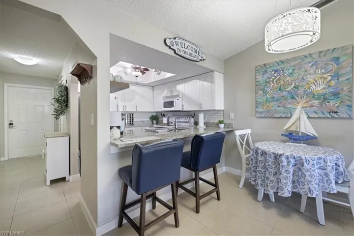 Kitchen featuring white cabinets, a textured ceiling, a kitchen bar, tasteful backsplash, and light stone countertops