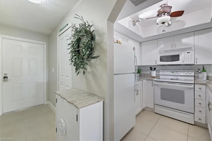 Kitchen featuring white appliances, white cabinets, light tile patterned floors, and a textured ceiling