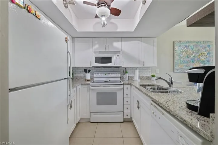 Kitchen featuring white appliances, white cabinetry, and light stone countertops