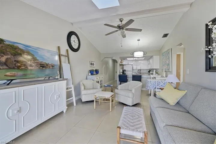 Living room with light tile patterned floors, a textured ceiling, a skylight, arched walkways, and a ceiling fan