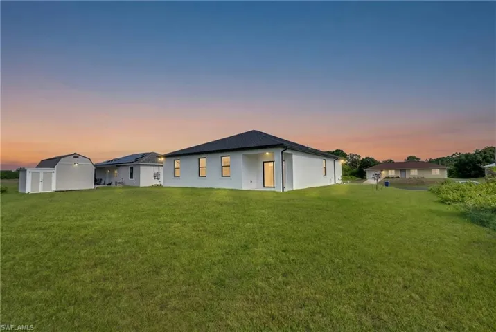 Expansive green lawn with a white stucco exterior and black shingle roof