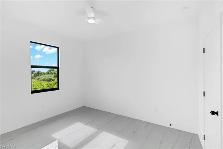 Bright interior room with a white ceiling fan, white walls, and a black-framed window