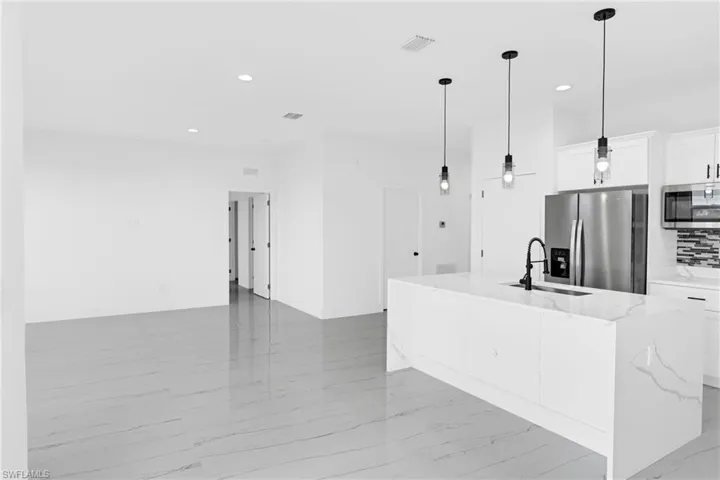 Spacious open-concept area featuring large format tile flooring, recessed lighting, and a kitchen island with a waterfall countertop