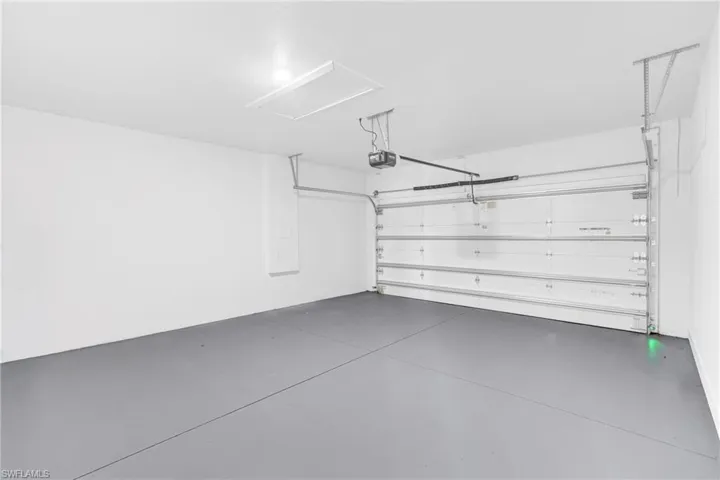 Garage featuring a gray floor, white walls, overhead lighting, and an automatic garage door opener