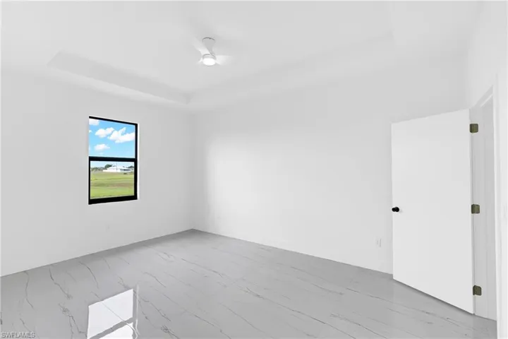 Spacious room featuring tray ceilings, a contemporary ceiling fan, and large format tile flooring