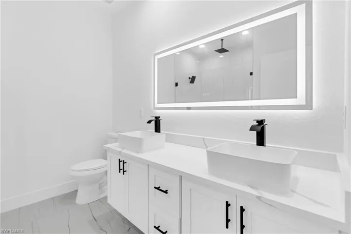 Bathroom vanity featuring dual vessel sinks with matte black faucets, white cabinetry with matte black hardware, and a white countertop
