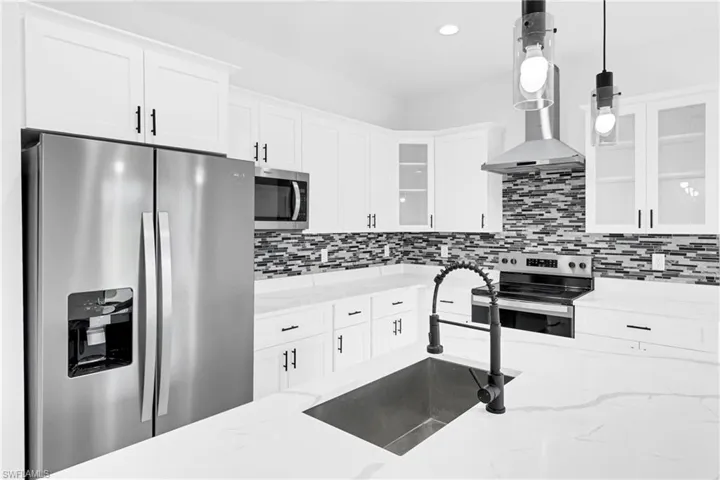 Kitchen featuring white cabinetry, stainless steel appliances, a multi-tone tile backsplash, quartz countertops, and a large kitchen island with an undermount sink and matte black faucet