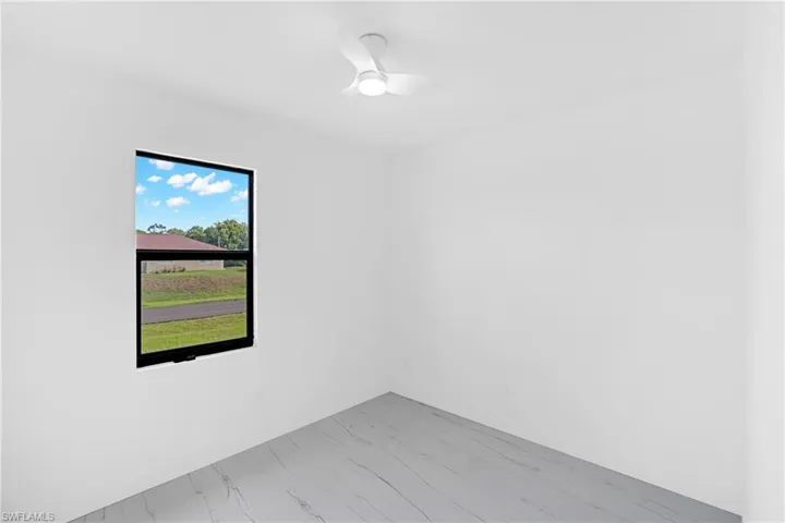 Bright interior space featuring a window with black trim, a contemporary ceiling fan with integrated lighting, white walls, and light-toned flooring