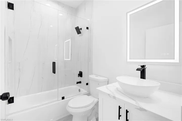 Bathroom featuring a white marble-patterned shower surround, clear glass shower enclosure, and matte black fixtures