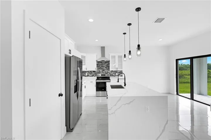 Modern kitchen featuring a waterfall island with a black sink, pendant lighting, stainless steel appliances, white cabinetry, and a mosaic tile backsplash