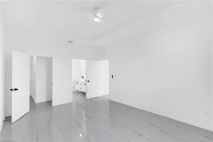 Spacious room featuring large format tile flooring, a tray ceiling, and a modern ceiling fan