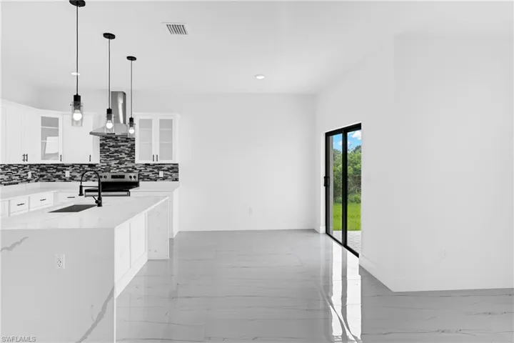 Open-concept kitchen featuring white cabinetry, a large island with a waterfall countertop, and a mosaic tile backsplash