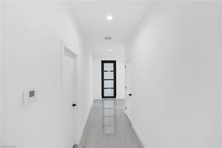 Modern hallway with recessed lighting, white walls, and a black-framed glass panel door