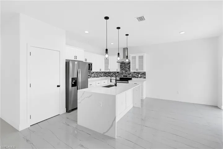 Modern kitchen featuring a waterfall island with an integrated sink, stainless steel appliances, white cabinetry, and a dark mosaic tile backsplash