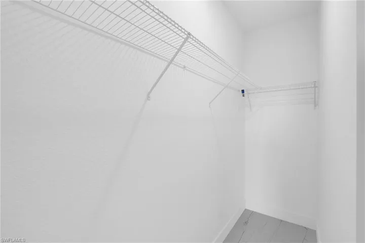 Walk-in closet featuring white wire shelving, white walls, white baseboards, and wood-finish flooring