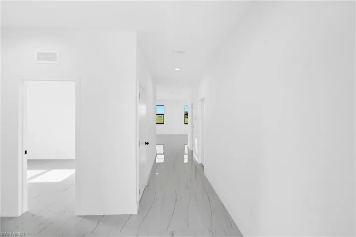 Long interior hallway featuring light-toned flooring with subtle veining, recessed lighting, and multiple doorways