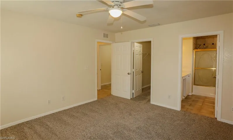 Unfurnished bedroom featuring light carpet, a walk in closet, a ceiling fan, and ensuite bath