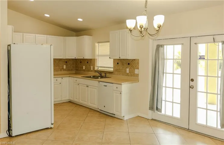Kitchen with white appliances, light countertops, backsplash, vaulted ceiling, and white cabinets