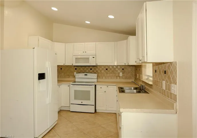 Kitchen with white appliances, lofted ceiling, light countertops, white cabinets, and recessed lighting